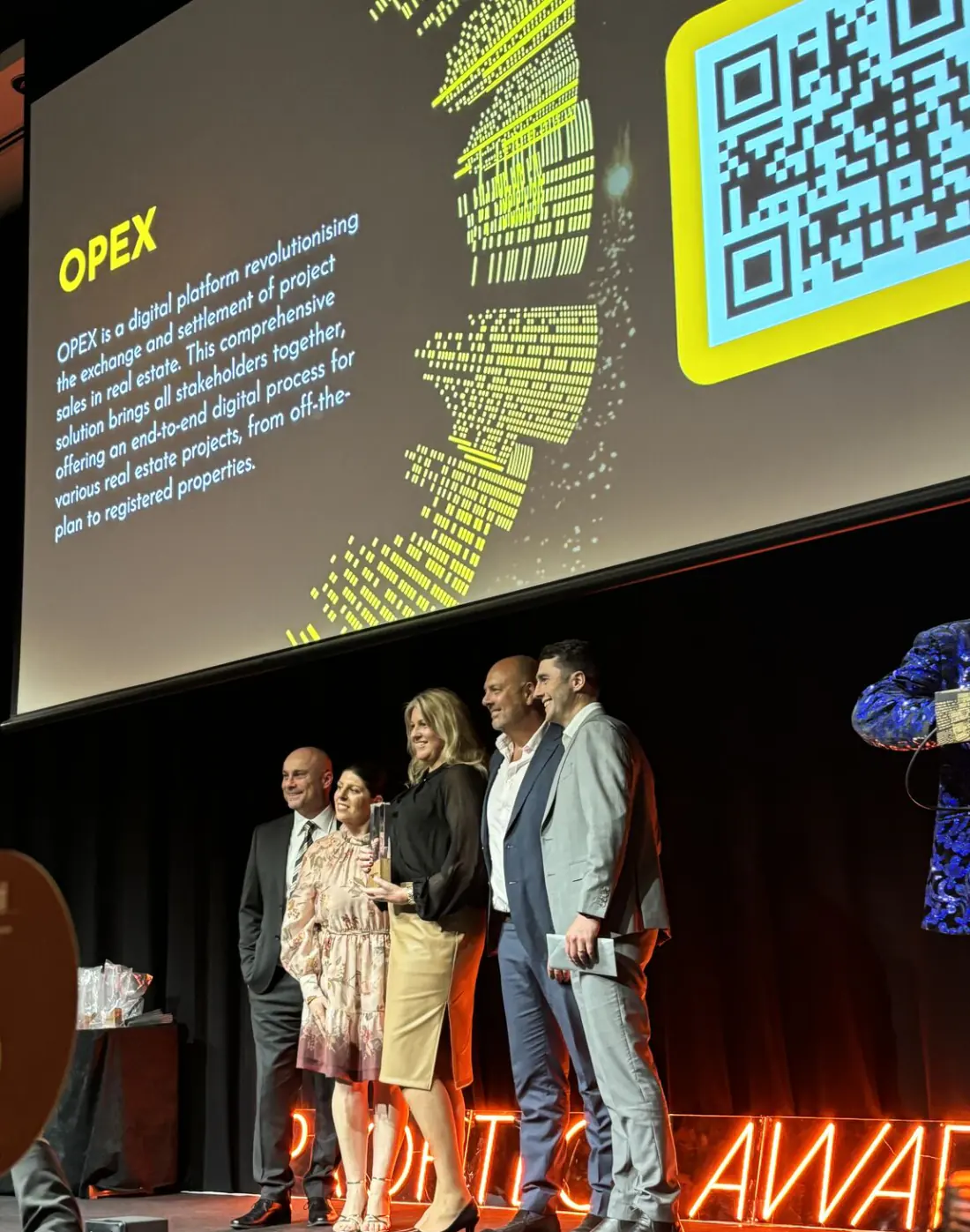 The OPEX team on stage at the PropTech Awards with their trophy, the OPEX submission projected behind them