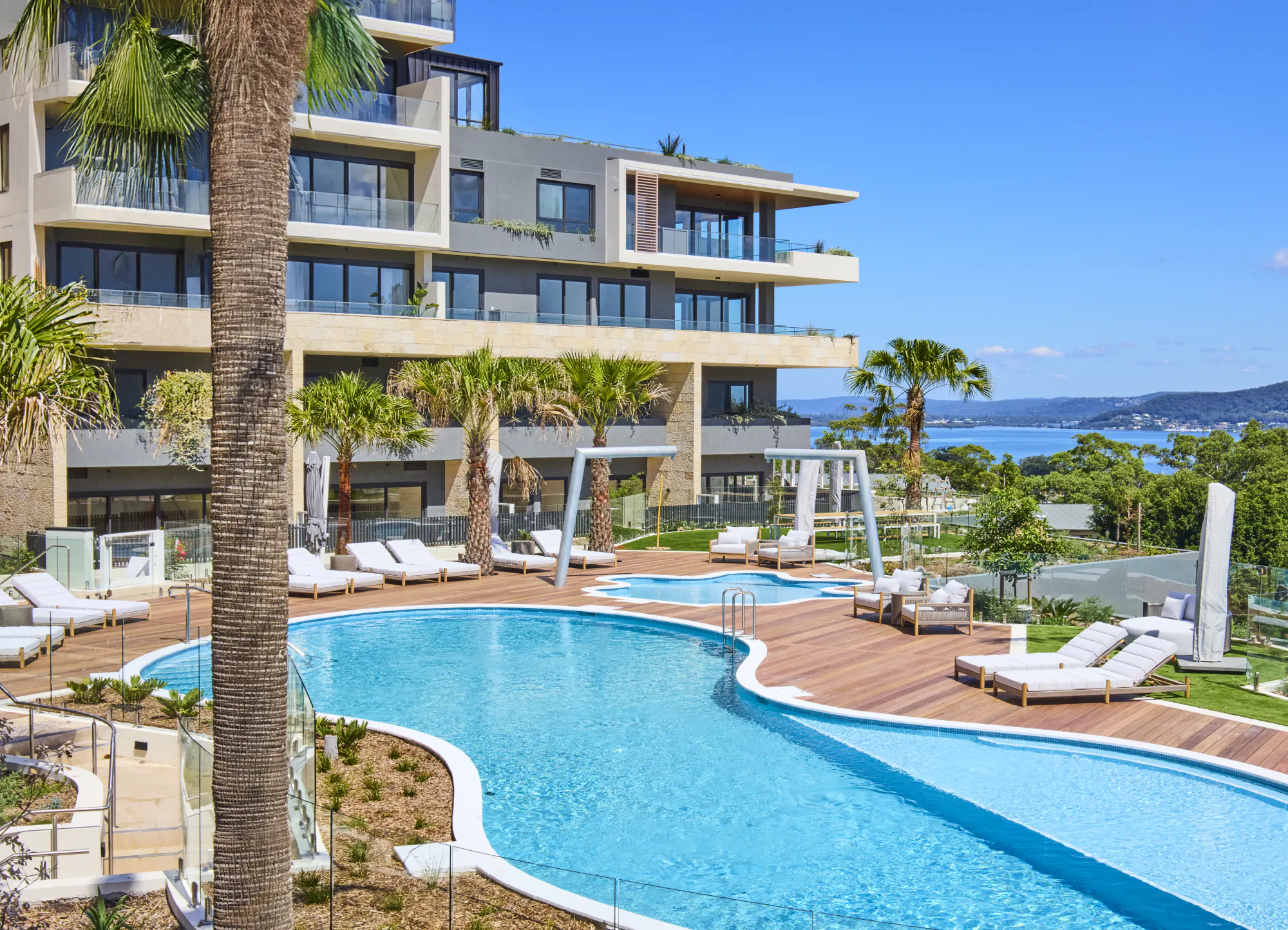 The completed resort pool and timber sun deck at Rumbalara Residences, palms and Brisbane Water beyond