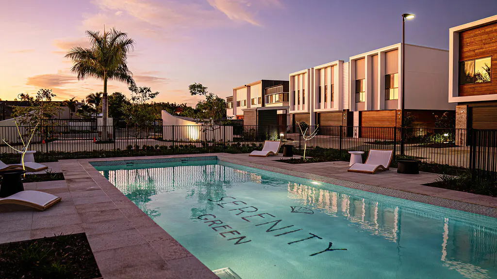 The Serenity Green pool and sun loungers at dusk, terrace homes lit behind
